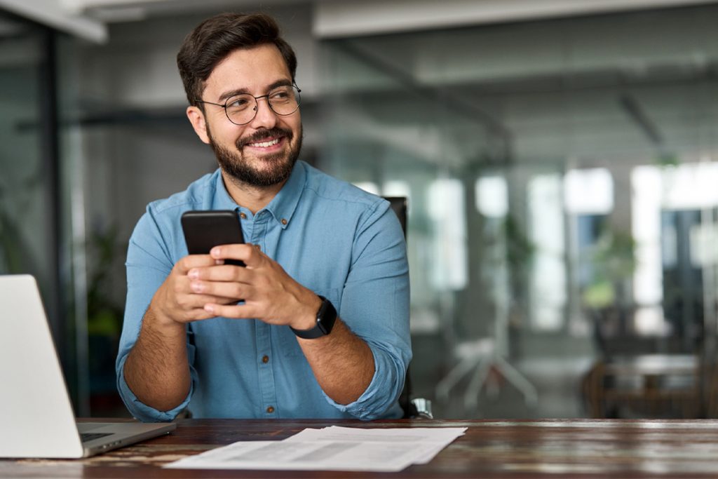 Smiling man at his desk with a laptop and cell phone